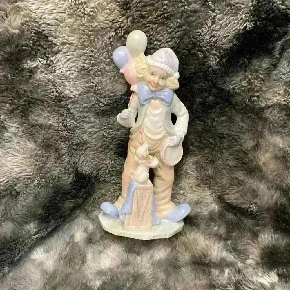Porcelain figurine of a clown holding balloons, with a  dog sitting on a box